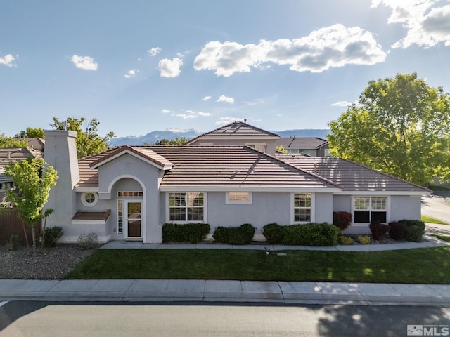 view of front of house featuring stucco siding, a tile roof, a front lawn, and a chimney