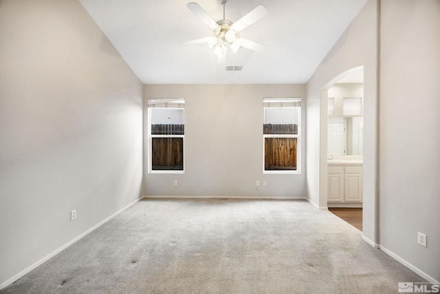 carpeted spare room featuring a ceiling fan, arched walkways, baseboards, and lofted ceiling