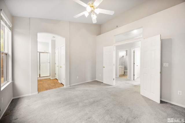 unfurnished bedroom with light colored carpet, arched walkways, connected bathroom, baseboards, and a ceiling fan