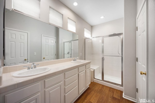 full bath featuring a shower stall, wood finished floors, double vanity, and recessed lighting