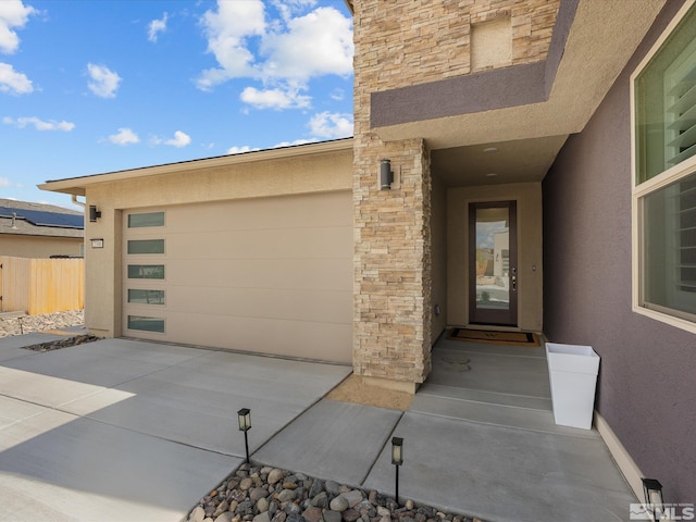entrance to property featuring stucco siding, concrete driveway, stone siding, and fence