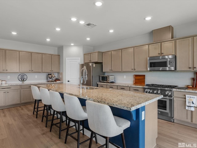 kitchen with stainless steel appliances, light brown cabinetry, an island with sink, a kitchen breakfast bar, and recessed lighting