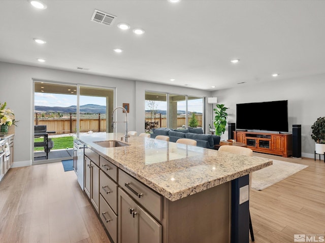 kitchen with a sink, a kitchen island with sink, light stone counters, light wood finished floors, and recessed lighting