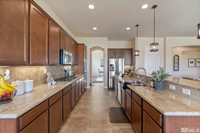 kitchen with arched walkways, appliances with stainless steel finishes, tasteful backsplash, light stone counters, and recessed lighting