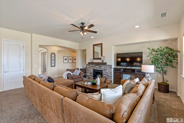 living area with carpet flooring, a ceiling fan, arched walkways, a brick fireplace, and baseboards
