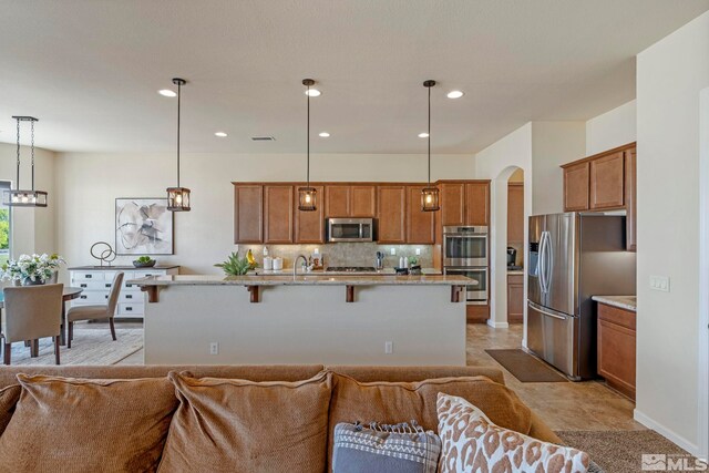 kitchen with stainless steel appliances, open floor plan, a breakfast bar, backsplash, and brown cabinetry