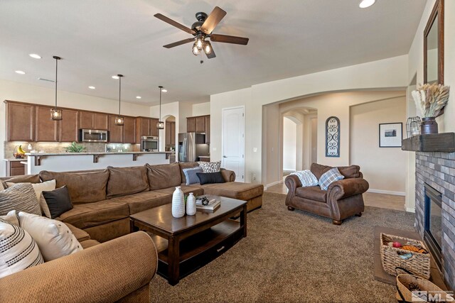 carpeted living room featuring arched walkways, a ceiling fan, a brick fireplace, recessed lighting, and baseboards