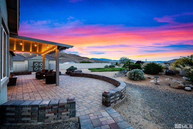 patio terrace at dusk with a shed, a mountain view, an outdoor structure, and a fenced backyard