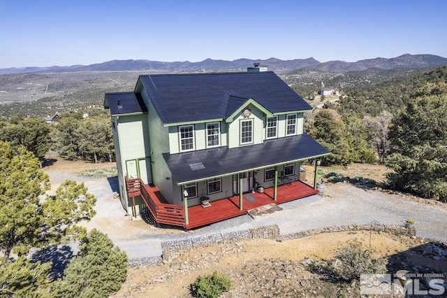 view of front of property featuring covered porch, a mountain view, a chimney, and gravel driveway