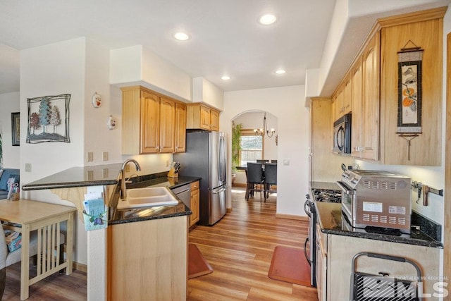 kitchen featuring a sink, stainless steel appliances, a peninsula, light wood-style floors, and a chandelier