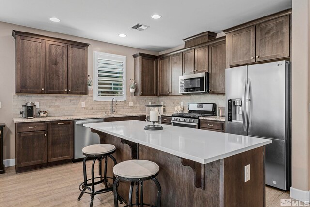 3325 Show Jumper Ln, Reno, NV 89521 - kitchen with stainless steel appliances, dark brown cabinetry, light wood-style flooring, a kitchen breakfast bar, and recessed lighting
