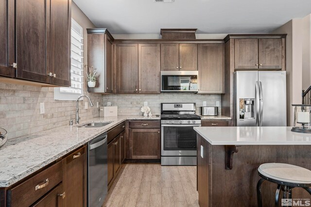 3325 Show Jumper Ln, Reno, NV 89521 - kitchen with appliances with stainless steel finishes, a sink, light wood finished floors, a breakfast bar area, and dark brown cabinets