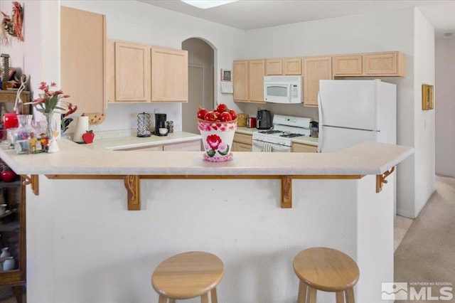 10010 Purple Sage Dr, Reno, NV 89506 - kitchen featuring white appliances, light brown cabinetry, a kitchen breakfast bar, and a peninsula