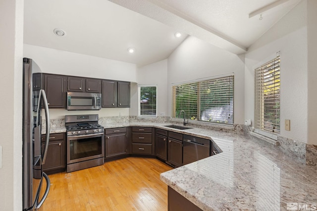 kitchen featuring stainless steel appliances, a sink, lofted ceiling, dark brown cabinetry, and light stone countertops