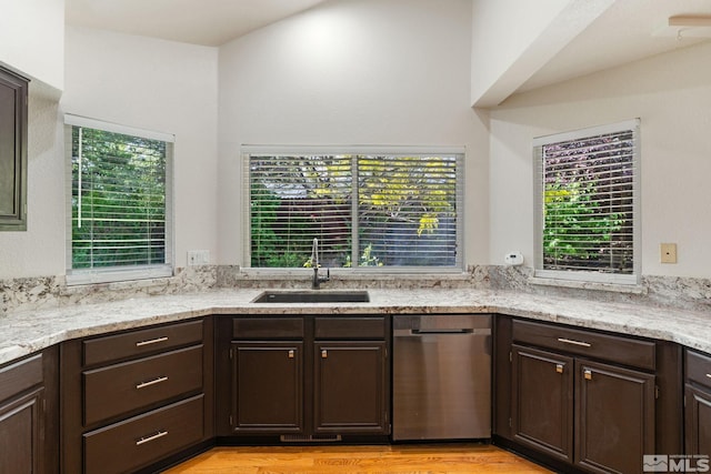 kitchen featuring a sink, stainless steel dishwasher, dark brown cabinetry, light wood-style flooring, and light stone countertops