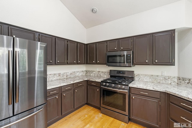 kitchen featuring stainless steel appliances, dark brown cabinetry, light wood finished floors, light stone countertops, and high vaulted ceiling