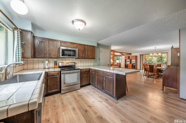 12565 Creek Crest Dr, Reno, NV 89511 - kitchen featuring appliances with stainless steel finishes, tile counters, a sink, a peninsula, and a textured ceiling