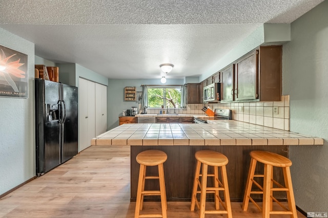 12565 Creek Crest Dr, Reno, NV 89511 - kitchen with appliances with stainless steel finishes, light wood-style floors, tasteful backsplash, a peninsula, and a textured ceiling