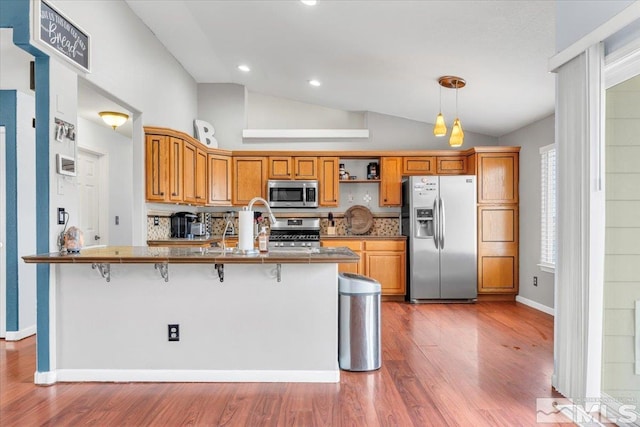 1310 Turf Ct, Fernley, NV 89408 - kitchen with appliances with stainless steel finishes, vaulted ceiling, a kitchen bar, wood finished floors, and backsplash