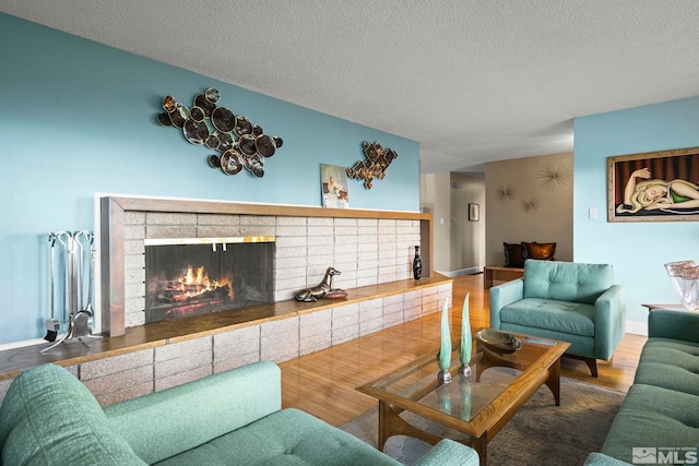 living room with wood finished floors, a brick fireplace, a textured ceiling, and baseboards