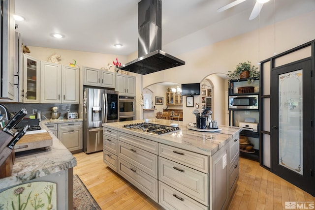 6525 Monticello Ct, Reno, NV 89519 - kitchen featuring appliances with stainless steel finishes, island exhaust hood, arched walkways, a sink, and light wood-style floors