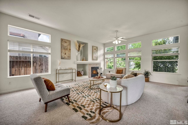living area with ceiling fan, carpet, and a tiled fireplace