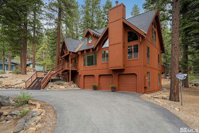 chalet / cabin with an attached garage, driveway, a chimney, a shingled roof, and stairs