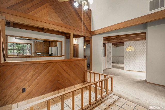 stairs with carpet, tile patterned flooring, ceiling fan, high vaulted ceiling, and a chandelier