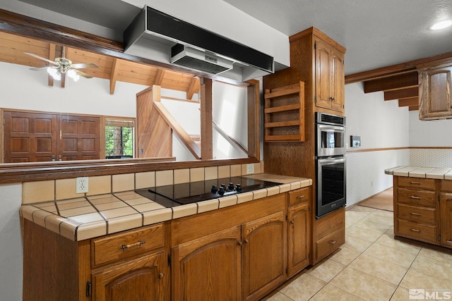 kitchen featuring open shelves, a ceiling fan, tile countertops, black electric cooktop, and double oven