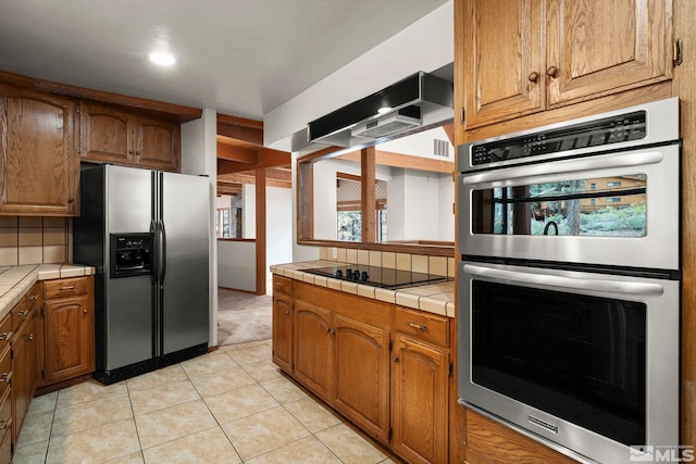 kitchen featuring appliances with stainless steel finishes, tile counters, light tile patterned floors, and brown cabinets