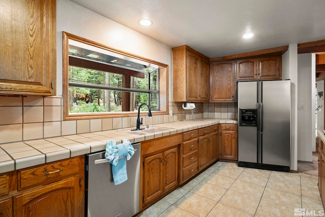 kitchen with appliances with stainless steel finishes, a sink, brown cabinets, decorative backsplash, and light tile patterned floors