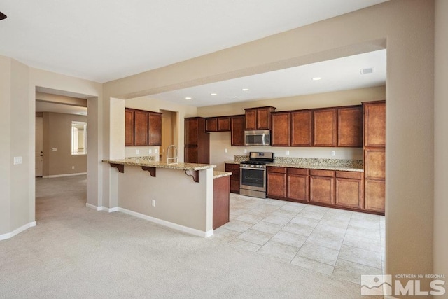 kitchen with appliances with stainless steel finishes, a sink, a kitchen breakfast bar, light stone countertops, and light colored carpet