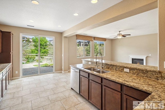 kitchen with a sink, dishwasher, baseboards, light stone countertops, and a ceiling fan