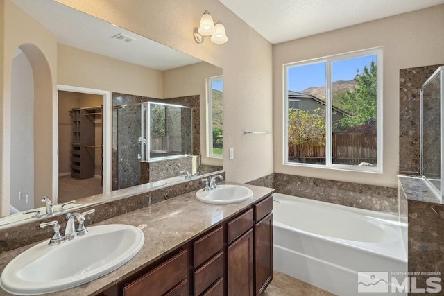 bathroom with a stall shower, a spacious closet, a bath, and double vanity
