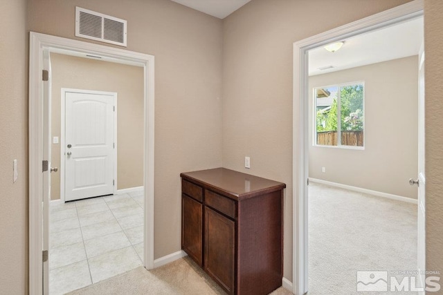 hallway with baseboards, light colored carpet, and light tile patterned floors