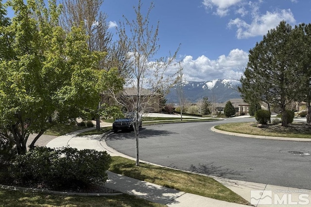 view of asphalt road with curbs, a mountain view, and sidewalks