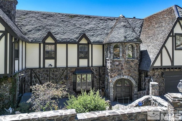 tudor home with stone siding, stucco siding, a chimney, and roof with shingles