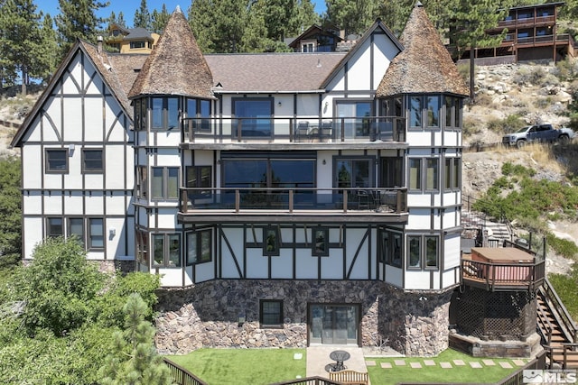 rear view of property with stucco siding, a balcony, and stone siding