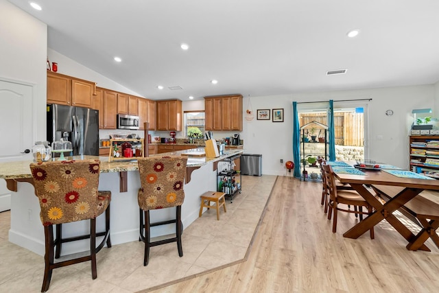 1390 Tule Peak Cir, Carson City, NV 89701 - kitchen with appliances with stainless steel finishes, brown cabinets, vaulted ceiling, a kitchen breakfast bar, and light stone counters