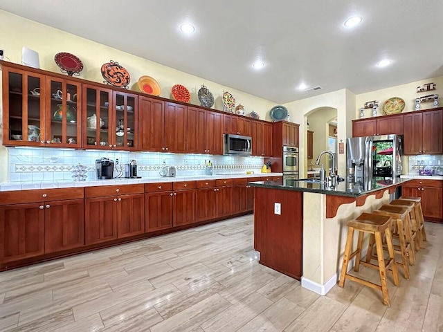 10555 Hampton Creek Dr, Reno, NV 89521 - kitchen featuring appliances with stainless steel finishes, a sink, arched walkways, a kitchen breakfast bar, and backsplash