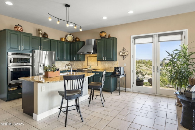 2698 Wind Feather Trl, Reno, NV 89511 - kitchen featuring stainless steel appliances, wall chimney exhaust hood, light stone countertops, backsplash, and green cabinetry