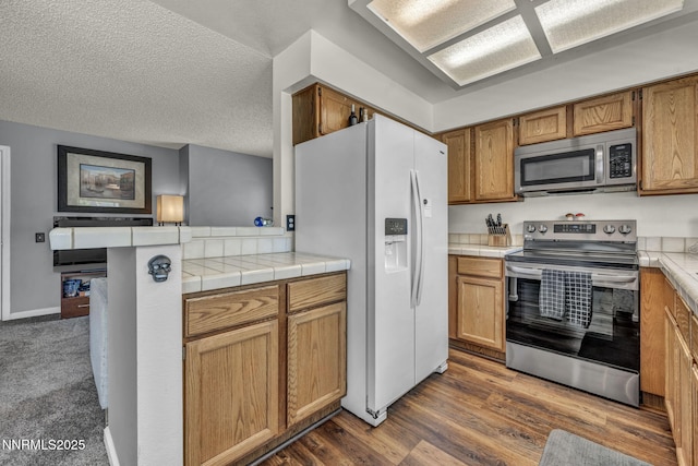 45 Stormy Ct, Sparks, NV 89436 - kitchen featuring appliances with stainless steel finishes, a peninsula, brown cabinets, a textured ceiling, and dark wood-style floors