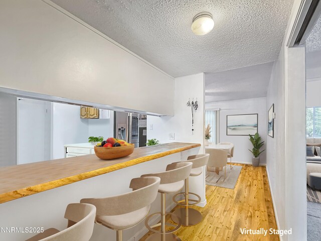 1714 Meadowvale Way, Sparks, NV 89431 - kitchen featuring a textured ceiling, stainless steel refrigerator with ice dispenser, light wood finished floors, a breakfast bar, and light countertops