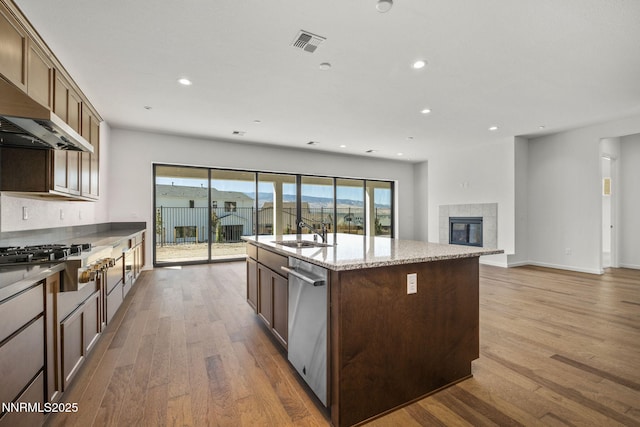 15025 Iron River Dr, Reno, NV 89521 - kitchen featuring appliances with stainless steel finishes, wood finished floors, a center island with sink, recessed lighting, and light stone countertops