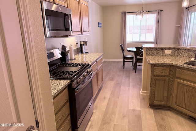 3185 Cliffrose Dr, Silver Springs, NV 89429 - kitchen featuring appliances with stainless steel finishes, light wood finished floors, a chandelier, brown cabinetry, and hanging light fixtures