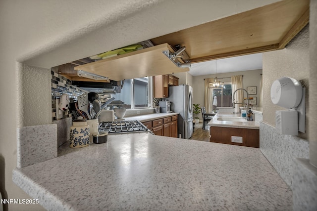 7442 Celeste Dr, Reno, NV 89511 - kitchen featuring brown cabinetry, a sink, freestanding refrigerator, ventilation hood, and pendant lighting