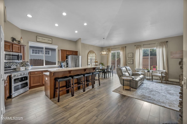 7442 Celeste Dr, Reno, NV 89511 - kitchen with stainless steel appliances, brown cabinets, a kitchen breakfast bar, a center island with sink, and light wood finished floors