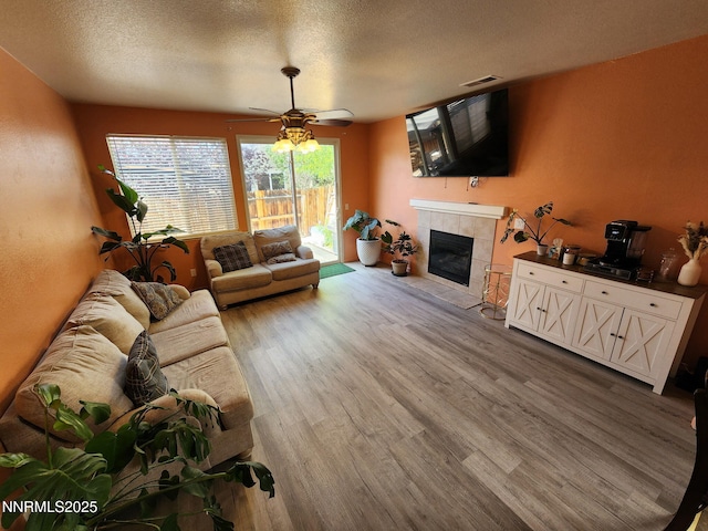 1224 Mountain Rose Dr, Fernley, NV 89408 - living room featuring wood finished floors, ceiling fan, a tiled fireplace, and a textured ceiling