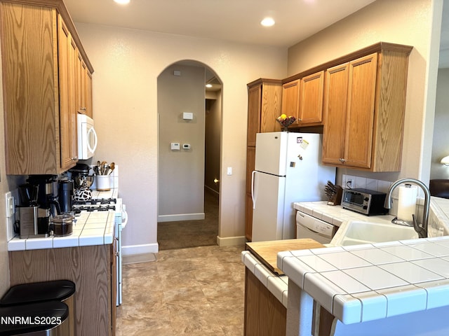 6680 Aston Cir, Sparks, NV 89436 - kitchen with white appliances, tile countertops, arched walkways, brown cabinets, and recessed lighting