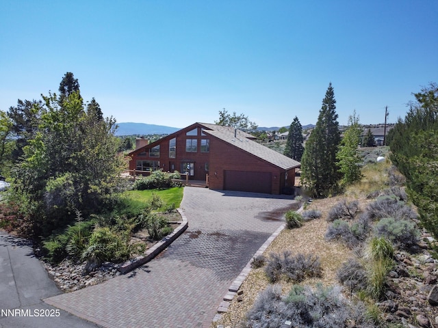 4360 Slide Mountain Cir, Reno, NV 89511 - view of side of home featuring decorative driveway, a chimney, an attached garage, and a mountain view